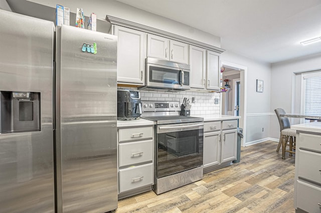 kitchen with stainless steel appliances, gray cabinets, backsplash, and light hardwood / wood-style flooring