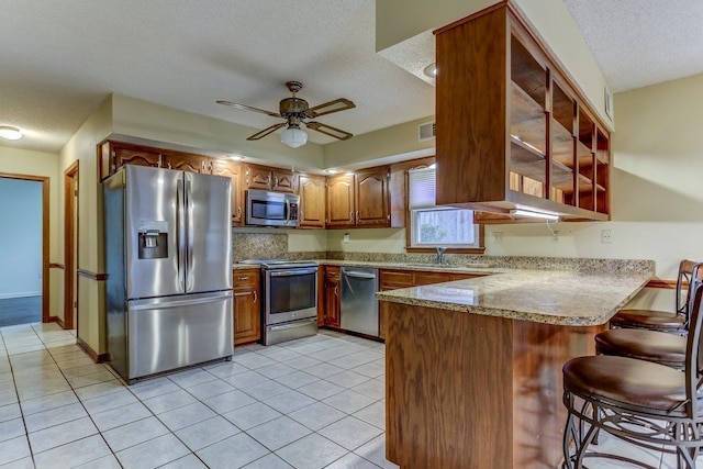 kitchen featuring light tile patterned flooring, kitchen peninsula, a textured ceiling, and appliances with stainless steel finishes