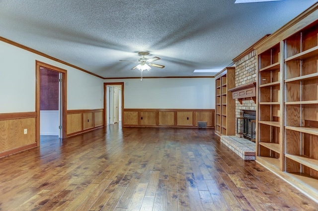 unfurnished living room featuring crown molding, a brick fireplace, a textured ceiling, dark hardwood / wood-style floors, and ceiling fan