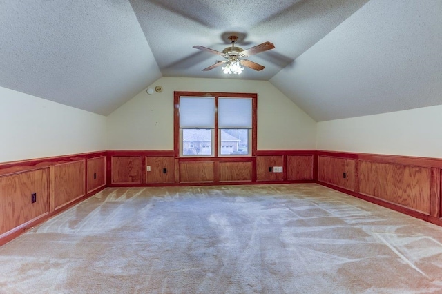 additional living space featuring light carpet, vaulted ceiling, and a textured ceiling