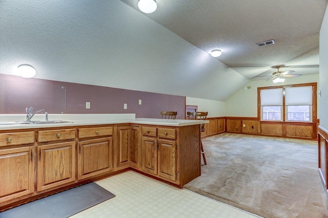 kitchen featuring sink, a breakfast bar area, vaulted ceiling, a textured ceiling, and kitchen peninsula