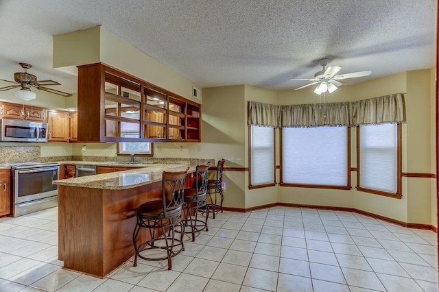 kitchen with light tile patterned flooring, sink, a kitchen breakfast bar, kitchen peninsula, and stainless steel appliances