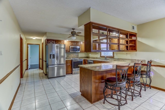 kitchen with stainless steel appliances, light tile patterned flooring, a kitchen bar, and kitchen peninsula