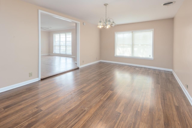 spare room with a notable chandelier and dark wood-type flooring