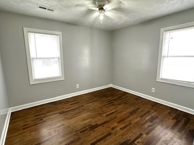 empty room with ceiling fan, dark hardwood / wood-style floors, a wealth of natural light, and a textured ceiling