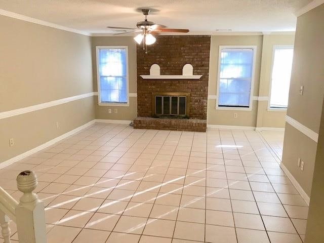 unfurnished living room featuring crown molding, ceiling fan, tile patterned floors, and a brick fireplace