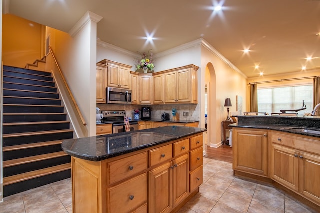 kitchen with tasteful backsplash, dark stone countertops, ornamental molding, a kitchen island, and stainless steel appliances