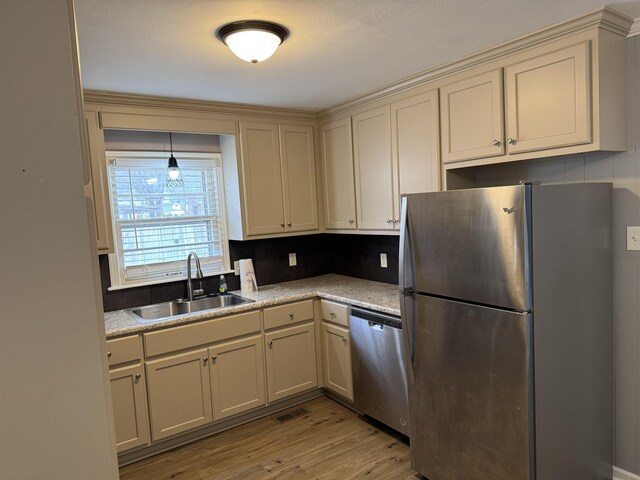 kitchen featuring appliances with stainless steel finishes, sink, light wood-type flooring, and cream cabinetry