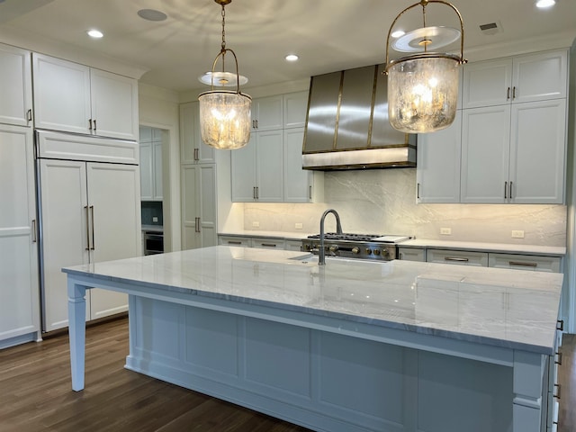 kitchen with a center island with sink, range hood, light stone counters, paneled built in fridge, and pendant lighting