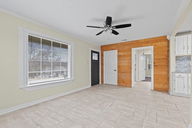 interior space featuring ceiling fan, wooden walls, and a textured ceiling