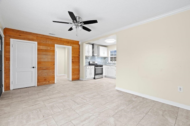 unfurnished living room featuring sink, wood walls, a textured ceiling, ornamental molding, and ceiling fan