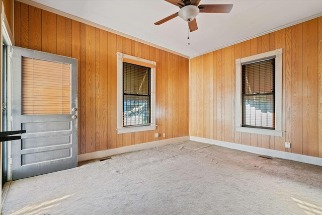 carpeted empty room featuring ceiling fan, ornamental molding, a healthy amount of sunlight, and wood walls