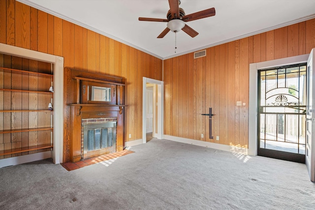 unfurnished living room featuring a fireplace, wooden walls, a healthy amount of sunlight, and carpet