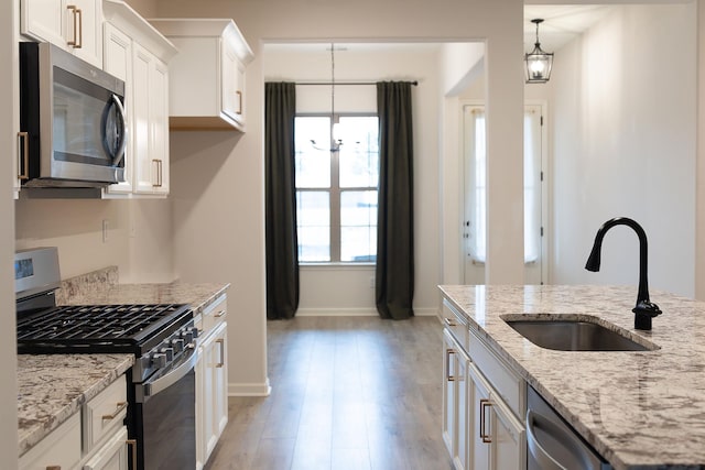 kitchen with appliances with stainless steel finishes, pendant lighting, white cabinetry, sink, and light stone countertops