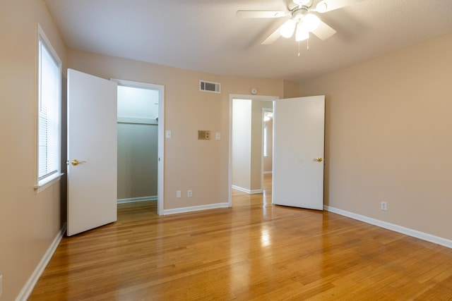 unfurnished bedroom with ceiling fan, a spacious closet, light wood-type flooring, and a closet