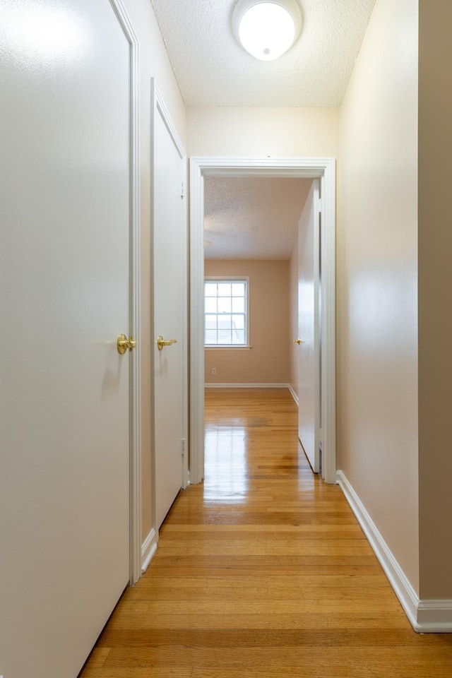 corridor with a textured ceiling and light wood-type flooring