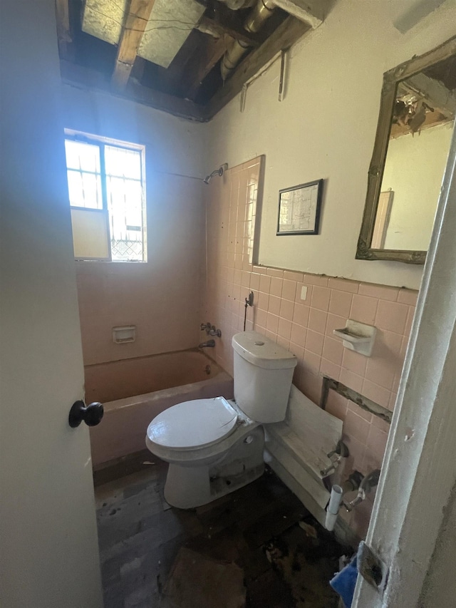 bathroom with toilet, tiled shower / bath combo, and tile walls