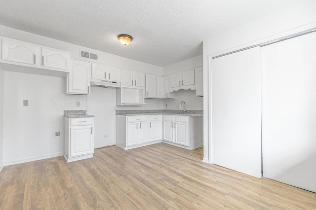 kitchen with sink, a textured ceiling, light hardwood / wood-style flooring, and white cabinets