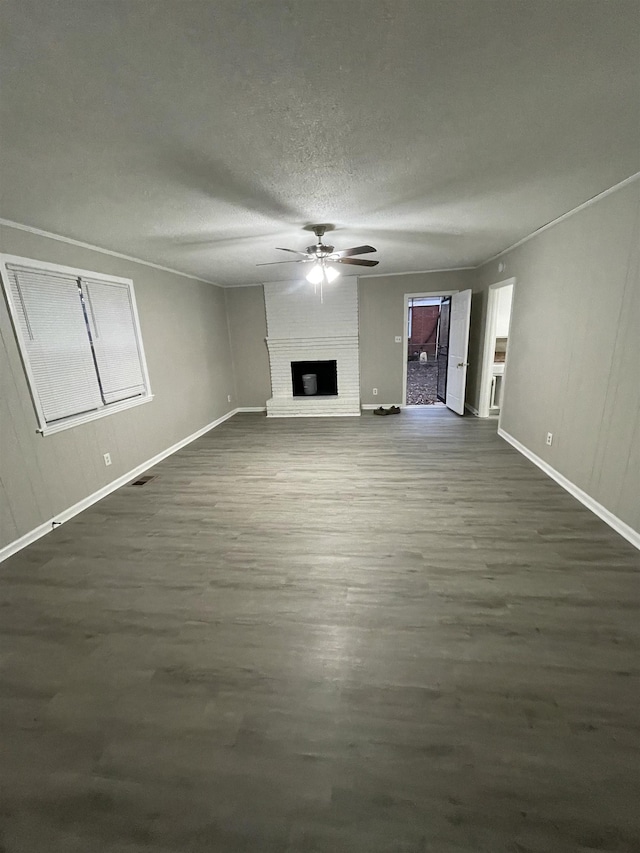 unfurnished living room with a brick fireplace, dark wood-type flooring, a textured ceiling, and ceiling fan