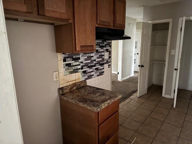 kitchen featuring extractor fan, dark stone countertops, light tile patterned flooring, and backsplash