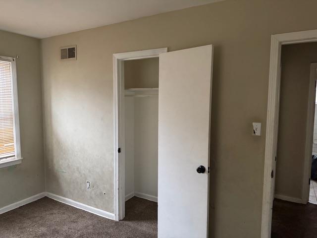 unfurnished bedroom with dark colored carpet and a closet