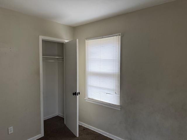 unfurnished bedroom with dark colored carpet and a closet