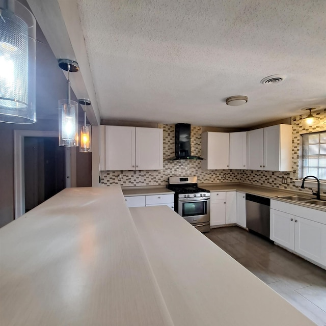 kitchen with decorative light fixtures, sink, white cabinets, stainless steel appliances, and wall chimney range hood