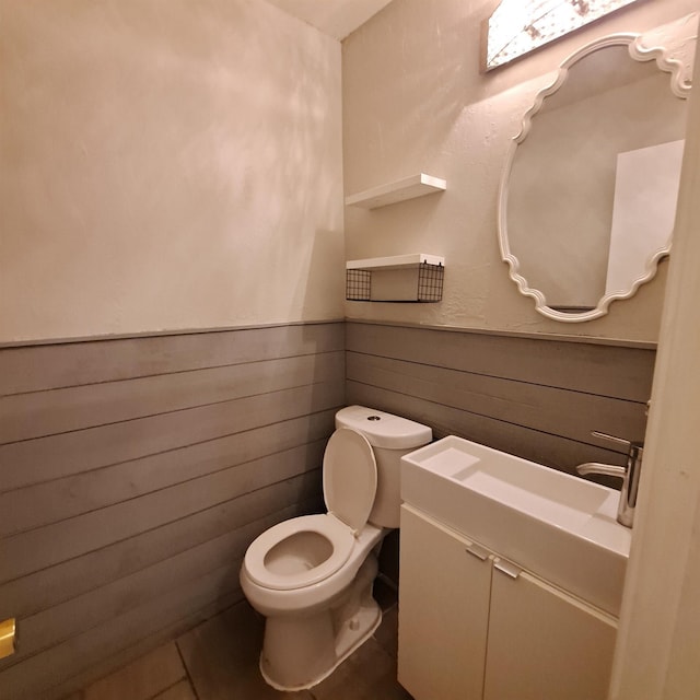 bathroom featuring toilet, vanity, and wood walls