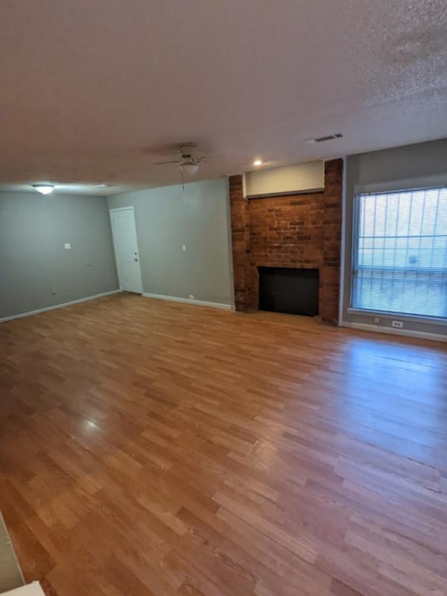 unfurnished living room featuring ceiling fan, hardwood / wood-style floors, a brick fireplace, and a textured ceiling