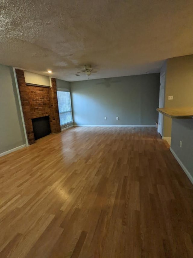 unfurnished living room featuring wood-type flooring, a wall mounted AC, a brick fireplace, a textured ceiling, and ceiling fan