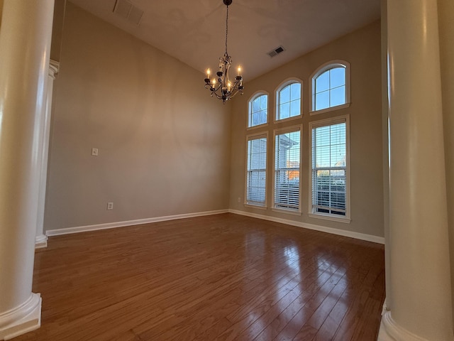 spare room featuring ornate columns, dark hardwood / wood-style floors, and a notable chandelier