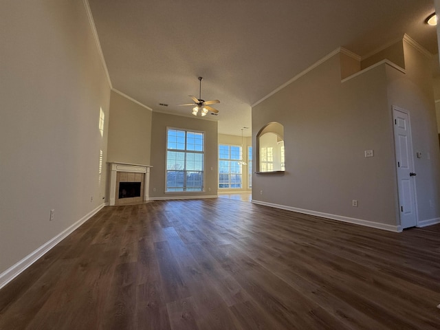 unfurnished living room with a tiled fireplace, crown molding, dark wood-type flooring, and ceiling fan