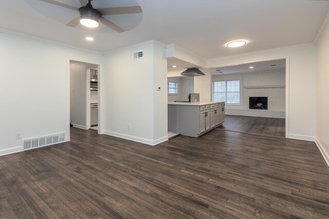 unfurnished living room featuring crown molding, ceiling fan, dark hardwood / wood-style flooring, and a brick fireplace