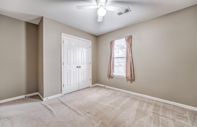 unfurnished bedroom featuring ceiling fan, light carpet, a textured ceiling, and a closet