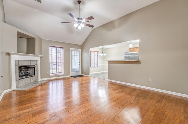 unfurnished living room featuring a tiled fireplace, high vaulted ceiling, ceiling fan with notable chandelier, and light wood-type flooring