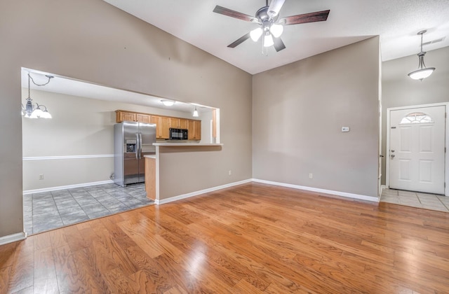 unfurnished living room featuring ceiling fan with notable chandelier and light wood-type flooring