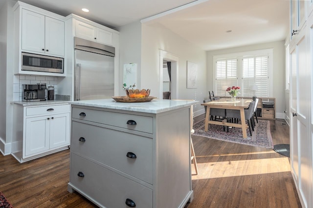 kitchen featuring dark hardwood / wood-style flooring, built in appliances, a center island, and white cabinets