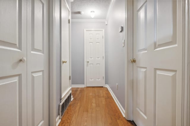 corridor with crown molding, light wood-type flooring, and a textured ceiling