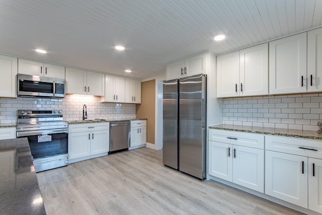 kitchen featuring light hardwood / wood-style flooring, backsplash, stainless steel appliances, white cabinets, and stone countertops