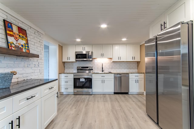 kitchen featuring light hardwood / wood-style flooring, appliances with stainless steel finishes, white cabinetry, dark stone countertops, and decorative backsplash