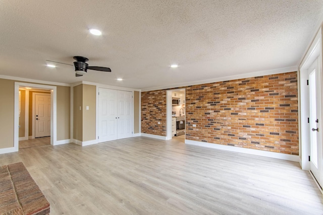 interior space with ceiling fan, brick wall, a textured ceiling, and light wood-type flooring