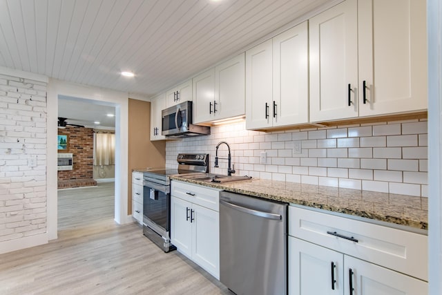 kitchen with sink, appliances with stainless steel finishes, white cabinetry, light stone counters, and tasteful backsplash