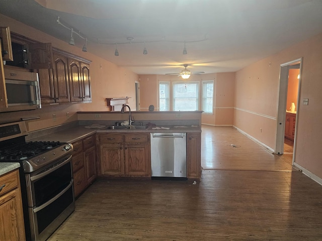 kitchen with rail lighting, sink, appliances with stainless steel finishes, dark hardwood / wood-style floors, and kitchen peninsula