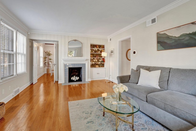 living room with crown molding, hardwood / wood-style floors, built in shelves, and a tiled fireplace