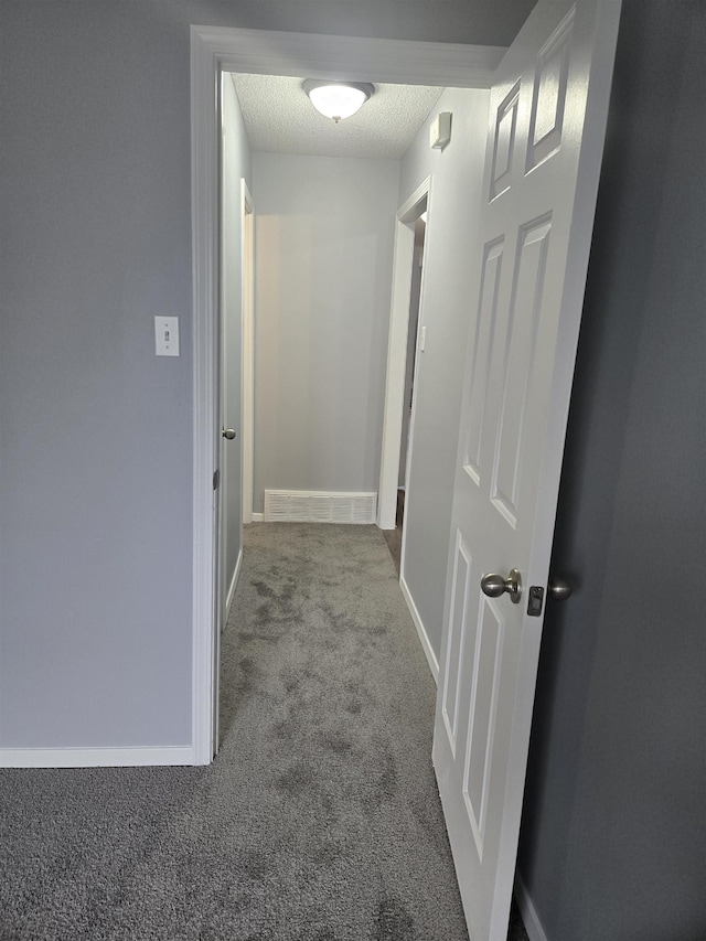 hall featuring carpet flooring and a textured ceiling