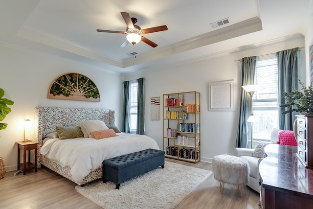 bedroom with light hardwood / wood-style flooring, ornamental molding, a raised ceiling, and ceiling fan