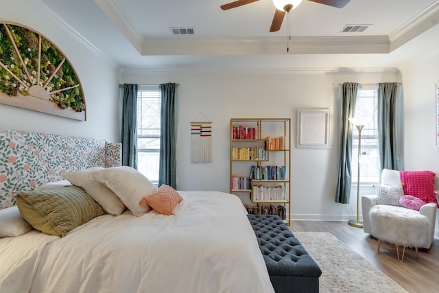 bedroom featuring multiple windows, a tray ceiling, ornamental molding, and light wood-type flooring