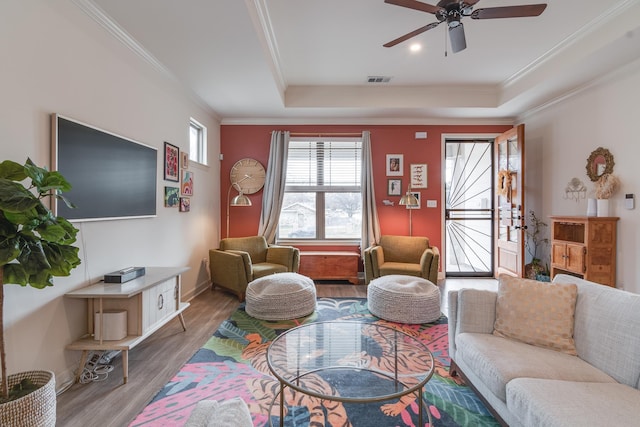 living room featuring a tray ceiling, wood-type flooring, and ornamental molding