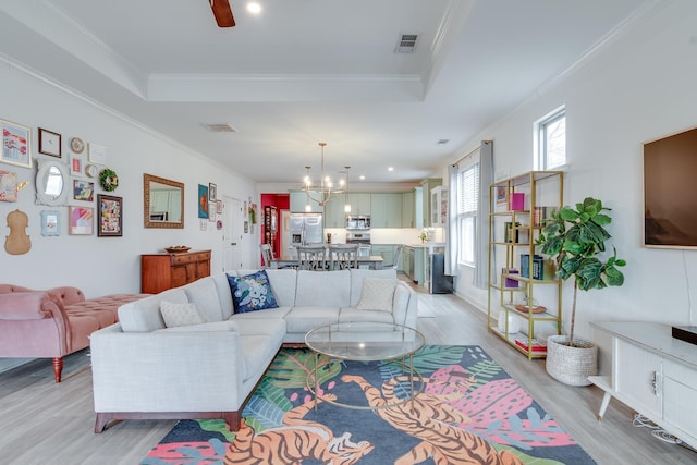 living room with a tray ceiling, ornamental molding, light hardwood / wood-style floors, and a chandelier