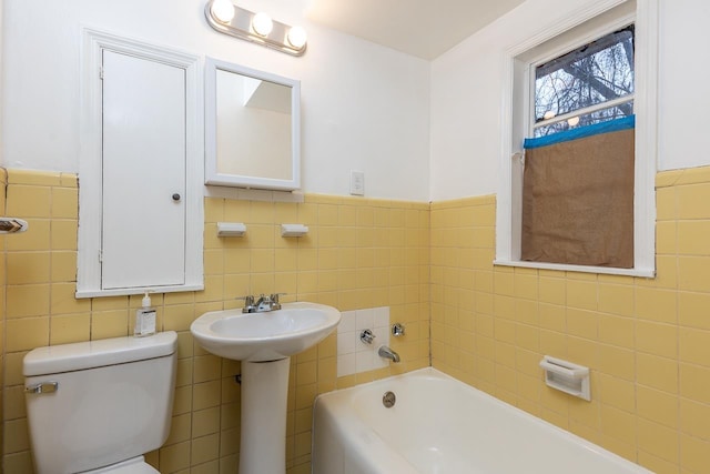 bathroom featuring tile walls, a tub to relax in, sink, and toilet